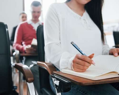 With notepad and pen in hands. Group of people at business conference in modern classroom at daytime.