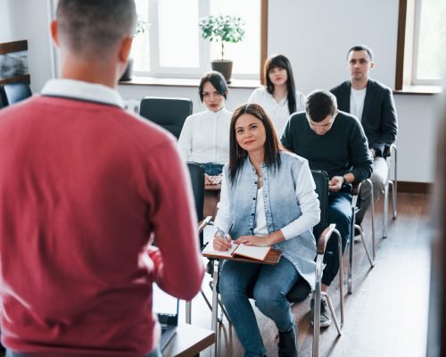 In red shirt. Group of people at business conference in modern classroom at daytime.
